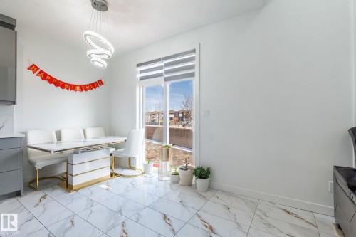 Spacious dining area featuring large format white tile flooring with brown veining, a full-height window, and a modern chandelier - 6607 50A Avenue, Beaumont, AB - Indoor