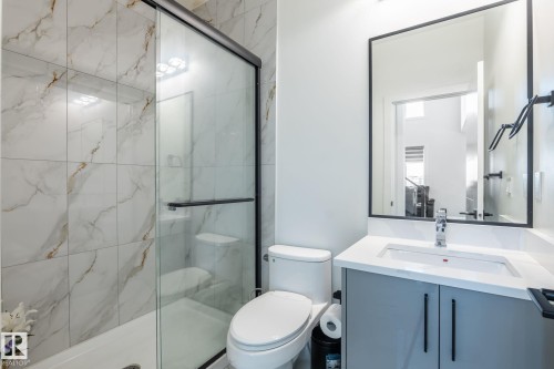 Bathroom featuring a frameless glass shower enclosure with a black frame, full-height marble-look tile surround, a built-in toilet, a vanity with a white countertop and integrated sink, and a black-framed mirror - 6607 50A Avenue, Beaumont, AB - Indoor Photo Showing Bathroom