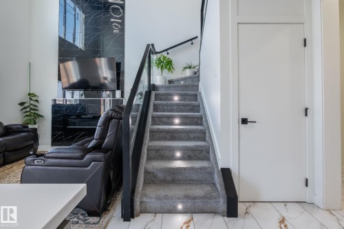Two-story living area featuring a carpeted staircase with integrated step lighting and a glass railing - 6607 50A Avenue, Beaumont, AB - Indoor Photo Showing Other Room