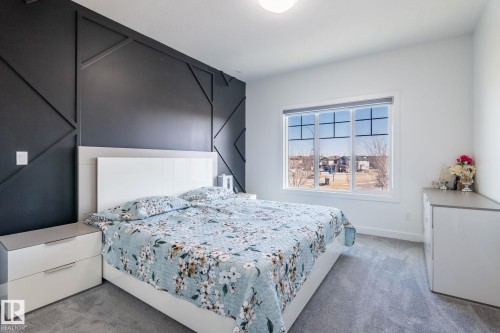 Spacious room featuring a dark accent wall with geometric paneling, light gray carpeting, and a large window providing ample natural light - 6607 50A Avenue, Beaumont, AB - Indoor Photo Showing Bedroom