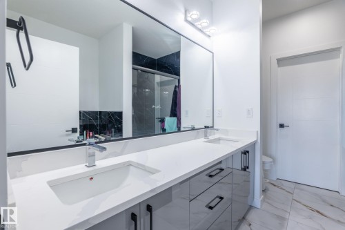 Spacious bathroom featuring a double vanity with integrated sinks, light-toned countertop, glossy gray cabinetry with black hardware, and large format floor tiling - 6607 50A Avenue, Beaumont, AB - Indoor Photo Showing Bathroom