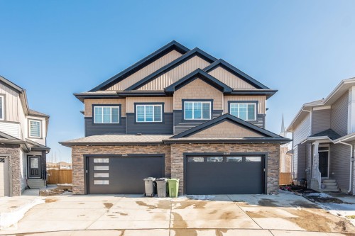 Modern duplex exterior with stone facade, dark siding, and contrasting tan shake accents - 6607 50A Avenue, Beaumont, AB - Outdoor With Facade