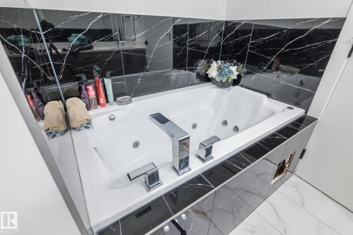 Deep soaking tub with polished chrome fixtures set against black marble-look tile - 6607 50A Avenue, Beaumont, AB - Indoor