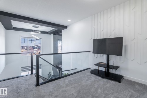 Upper-level landing featuring glass railings with matte black framing, plush gray carpeting, and a textured accent wall - 6607 50A Avenue, Beaumont, AB - Indoor Photo Showing Other Room