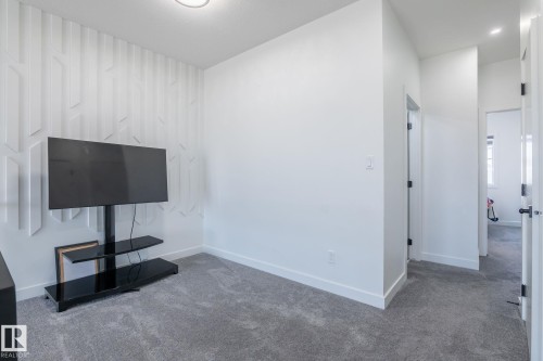 Room featuring an accent wall with geometric paneling, light gray carpeting, crisp white walls, and bright overhead lighting - 6607 50A Avenue, Beaumont, AB - Indoor Photo Showing Other Room