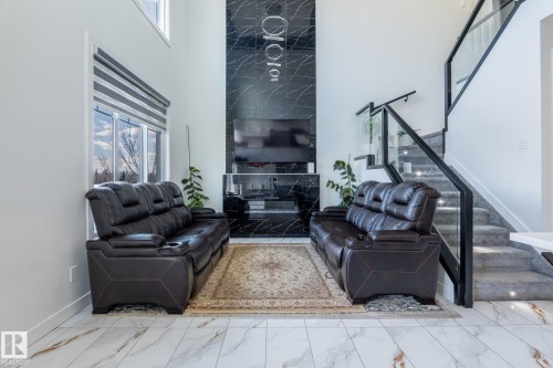 Two-story living area featuring a black marble-finish accent wall with integrated lighting, a contemporary glass and metal staircase, large windows with horizontal blinds, and large format marble-finish floor tiles - 6607 50A Avenue, Beaumont, AB - Indoor