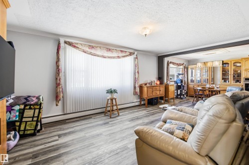 Spacious living area featuring wood-finish flooring, a large window with vertical blinds, and crown molding - 3920 35A Avenue, Red Deer, AB - Indoor Photo Showing Living Room