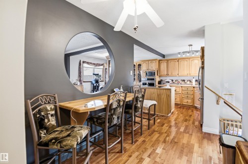 Open-concept living space featuring wood-finish flooring, a wall-mounted breakfast bar, a circular wall cutout, and a kitchen with light wood cabinetry and built-in appliances - 3920 35A Avenue, Red Deer, AB - Indoor