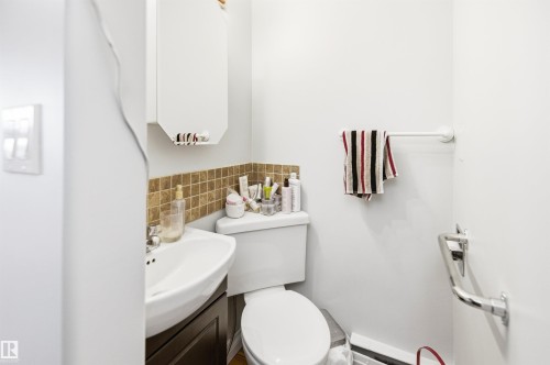 Compact powder room featuring a wall-mounted vanity with integrated sink, a white toilet, and a tiled backsplash - 3920 35A Avenue, Red Deer, AB - Indoor Photo Showing Bathroom