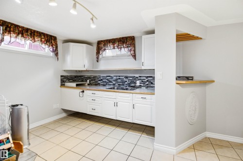 Kitchenette featuring white cabinetry, light wood-finish countertops, a mosaic tile backsplash, and a double basin sink - 3920 35A Avenue, Red Deer, AB - Indoor