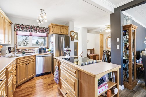 Well-appointed kitchen featuring wood-finish cabinetry, stainless steel appliances, a corner sink with window, a central island with a built-in cooktop, and wood-finish flooring - 3920 35A Avenue, Red Deer, AB - Indoor Photo Showing Kitchen With Double Sink