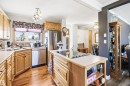 Well-appointed kitchen featuring wood-finish cabinetry, stainless steel appliances, a corner sink with window, a central island with a built-in cooktop, and wood-finish flooring - 3920 35A Avenue, Red Deer, AB  - Indoor Photo Showing Kitchen With Double Sink 