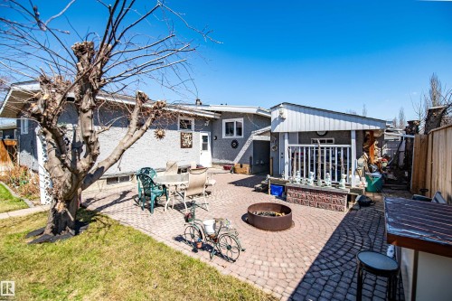 Expansive backyard featuring a circular paver patio, a built-in fire pit, and a covered porch with white railing - 3920 35A Avenue, Red Deer, AB - Outdoor