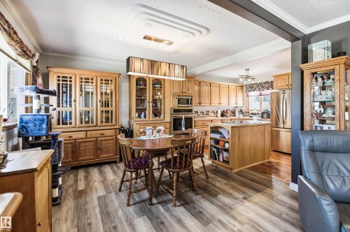 Spacious kitchen and dining area featuring wood-finish flooring, light wood cabinetry, a central kitchen island, stainless steel appliances, and a tray ceiling with recessed lighting - 3920 35A Avenue, Red Deer, AB - Indoor