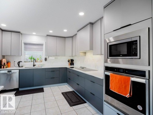Modern kitchen featuring two-tone cabinetry, stainless steel appliances, a built-in microwave and oven, a black faucet, and patterned tile flooring - 5701 Rue Eaglemont, Beaumont, AB - Indoor Photo Showing Kitchen With Upgraded Kitchen