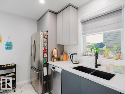 Modern kitchen with light gray upper and dark gray lower cabinetry, featuring a double basin sink with a matte black faucet - 5701 Rue Eaglemont, Beaumont, AB - Indoor Photo Showing Kitchen With Double Sink