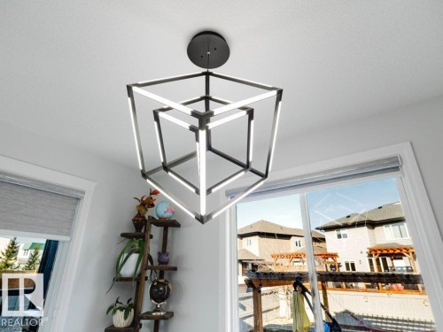 Modern geometric chandelier with integrated LED lighting, white ceiling, and a window with a roller shade - 5701 Rue Eaglemont, Beaumont, AB - Indoor Photo Showing Other Room