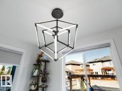 Modern geometric chandelier with integrated LED lighting, white ceiling, and a window with a roller shade - 