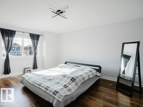 Spacious room featuring wood-finish flooring, a large window, white walls, and a contemporary ceiling light fixture - 5701 Rue Eaglemont, Beaumont, AB - Indoor Photo Showing Bedroom