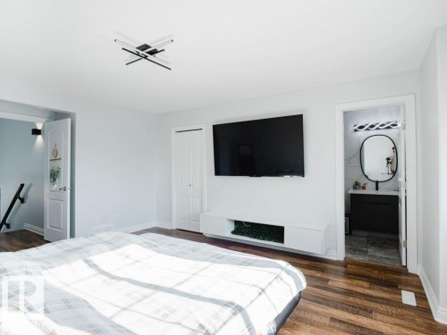 Spacious room featuring wood-finish flooring, a modern ceiling light fixture, and a wall-mounted media console - 5701 Rue Eaglemont, Beaumont, AB - Indoor Photo Showing Bedroom