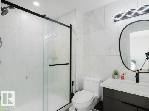 Modern bathroom featuring a frameless glass shower enclosure with matte black hardware, large format wall tiling, a contemporary vanity with an integrated sink, and an oval mirror with a black frame - 5701 Rue Eaglemont, Beaumont, AB - Indoor Photo Showing Bathroom