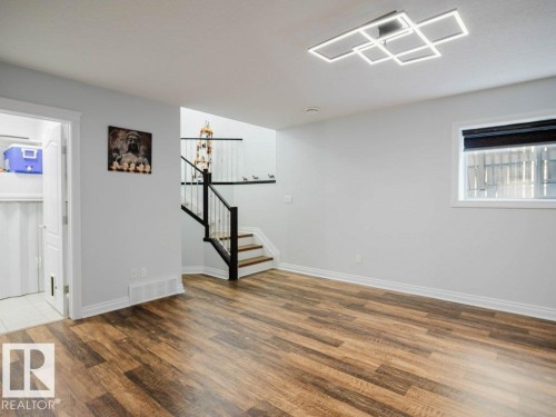 Spacious room featuring wood-finish flooring, white baseboards, and a contemporary geometric ceiling light fixture - 5701 Rue Eaglemont, Beaumont, AB - Indoor Photo Showing Other Room