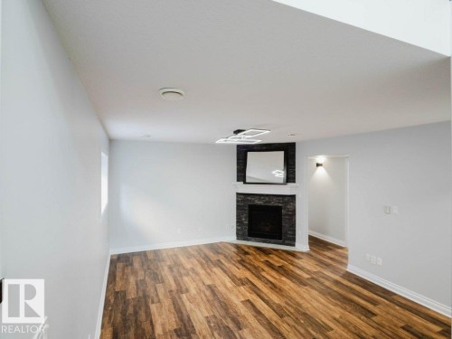 Living area featuring a dark stone-clad fireplace with a white mantel, wood-finish flooring, recessed lighting, and a modern ceiling light fixture - 5701 Rue Eaglemont, Beaumont, AB - Indoor Photo Showing Other Room With Fireplace