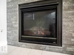 Modern fireplace featuring a black metal frame, gray stacked stone surround, and light tile flooring - 