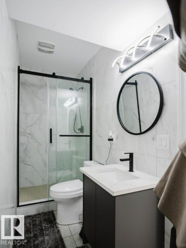Bathroom featuring a black-framed glass shower enclosure, white porcelain toilet, and a vanity with a white countertop and dark cabinetry - 5701 Rue Eaglemont, Beaumont, AB - Indoor Photo Showing Bathroom
