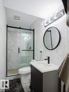 Bathroom featuring a black-framed glass shower enclosure, white porcelain toilet, and a vanity with a white countertop and dark cabinetry - 