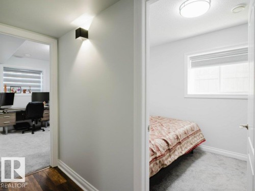Hallway featuring a contemporary wall sconce providing upward and downward illumination, wood-finish flooring, and crisp white baseboards - 5701 Rue Eaglemont, Beaumont, AB - Indoor