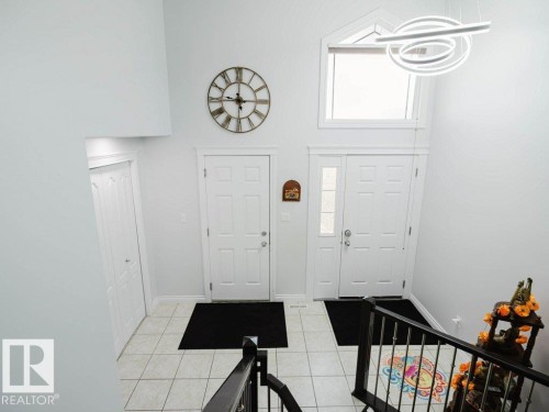 Two-story entryway featuring a contemporary chandelier, transom window, ceramic tile flooring, and a baluster staircase - 5701 Rue Eaglemont, Beaumont, AB - Indoor Photo Showing Other Room
