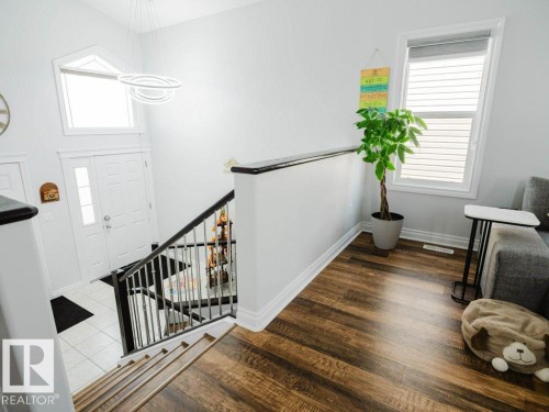 Open-concept entry foyer featuring a striking contemporary light fixture, a large transom window, and a white paneled entry door with a frosted glass insert - 5701 Rue Eaglemont, Beaumont, AB - Indoor Photo Showing Other Room