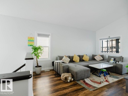 Spacious living area featuring wood-finish flooring, white walls, and multiple windows with blinds - 5701 Rue Eaglemont, Beaumont, AB - Indoor Photo Showing Living Room