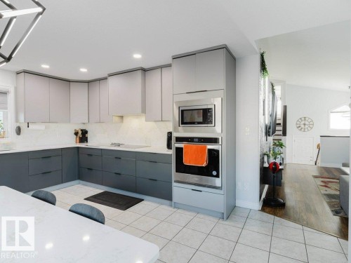 Contemporary kitchen featuring two-tone cabinetry, integrated stainless steel appliances including a wall oven and microwave, white quartz countertops, and a full tile backsplash - 5701 Rue Eaglemont, Beaumont, AB - Indoor Photo Showing Kitchen