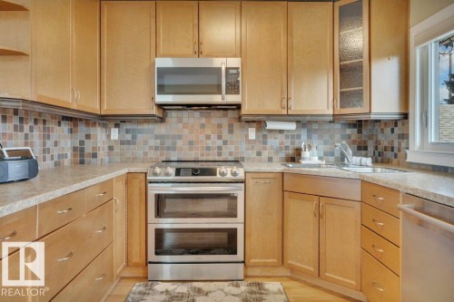 Kitchen featuring light wood cabinetry, a mosaic tile backsplash, stainless steel appliances including a double oven range and microwave, ample counter space, and an undermount sink - 10633 St Gabriel School Road, Edmonton, AB - Indoor Photo Showing Kitchen