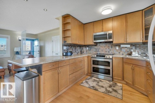 Kitchen featuring wood-finish cabinetry, stainless steel appliances including a double oven range and microwave, a mosaic tile backsplash, and a countertop island with seating space - 10633 St Gabriel School Road, Edmonton, AB - Indoor Photo Showing Kitchen