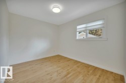Bright room featuring light wood-finish flooring, white walls, and a single window with a privacy shade - 