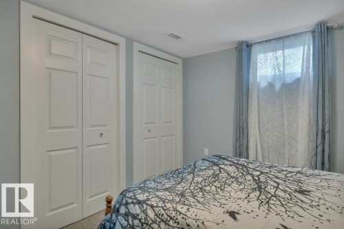 Two white bi-fold closets flank a window with sheer and patterned curtains - 10633 St Gabriel School Road, Edmonton, AB - Indoor Photo Showing Bedroom