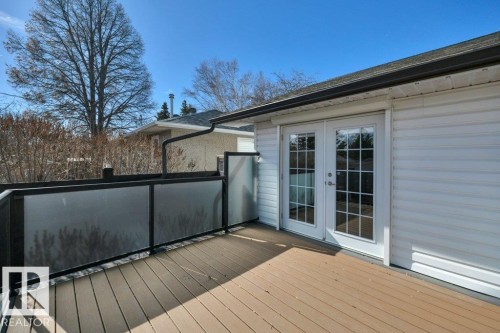 Spacious outdoor deck featuring composite decking, frosted glass railings with black metal frames, and white French doors - 10633 St Gabriel School Road, Edmonton, AB - Outdoor With Deck Patio Veranda With Exterior