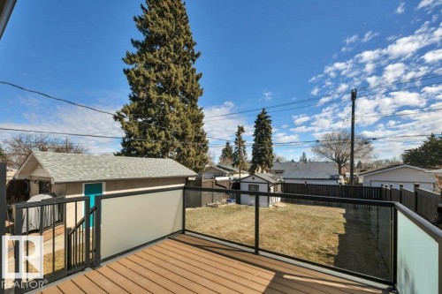 Spacious backyard featuring a composite deck with glass panel railings, a detached garage with a light blue door, and a separate storage shed - 10633 St Gabriel School Road, Edmonton, AB - Outdoor