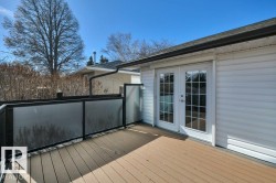 Spacious outdoor deck featuring composite decking, frosted glass railings with black metal frames, and white French doors - 