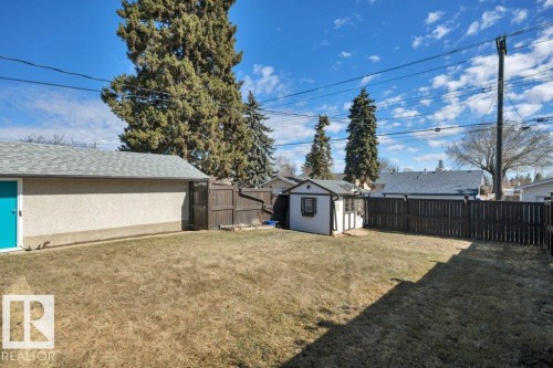 Expansive backyard featuring a detached garage with a turquoise door, a separate storage shed, and a privacy fence - 10633 St Gabriel School Road, Edmonton, AB - Outdoor