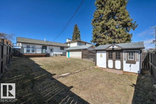 Expansive backyard featuring a white storage shed with brown trim, a rear deck with glass panel railing, and a fully fenced perimeter - 10633 St Gabriel School Road, Edmonton, AB - Outdoor