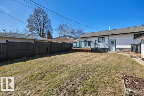 Expansive backyard featuring a large wood deck with glass panel railing, white vinyl siding, a dark privacy fence, and a raised garden bed - 10633 St Gabriel School Road, Edmonton, AB - Outdoor With Deck Patio Veranda