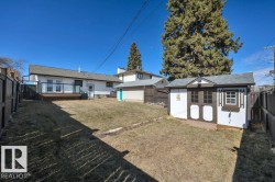 Expansive backyard featuring a white storage shed with brown trim, a rear deck with glass panel railing, and a fully fenced perimeter - 