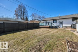 Expansive backyard featuring a large wood deck with glass panel railing, white vinyl siding, a dark privacy fence, and a raised garden bed - 