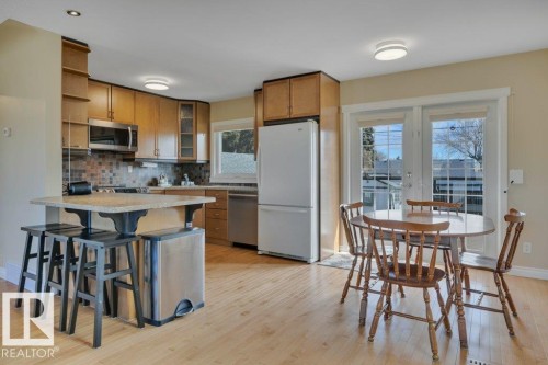 Bright kitchen featuring light wood-finish flooring, wood cabinetry, stainless steel appliances, and a tiled backsplash - 10633 St Gabriel School Road, Edmonton, AB - Indoor