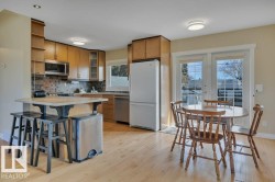Bright kitchen featuring light wood-finish flooring, wood cabinetry, stainless steel appliances, and a tiled backsplash - 