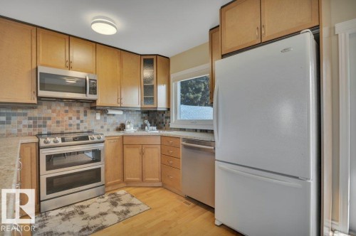 Full kitchen featuring wood cabinetry, stainless steel appliances including a double oven range and microwave, light-toned countertops, and a tiled backsplash - 10633 St Gabriel School Road, Edmonton, AB - Indoor Photo Showing Kitchen